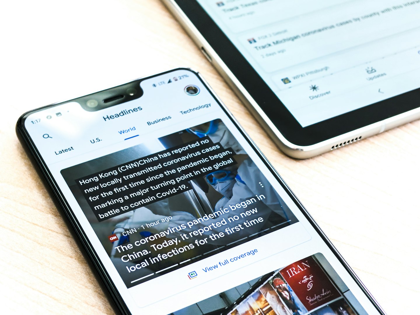 Smartphone and tablet displaying news apps on a wooden desk.