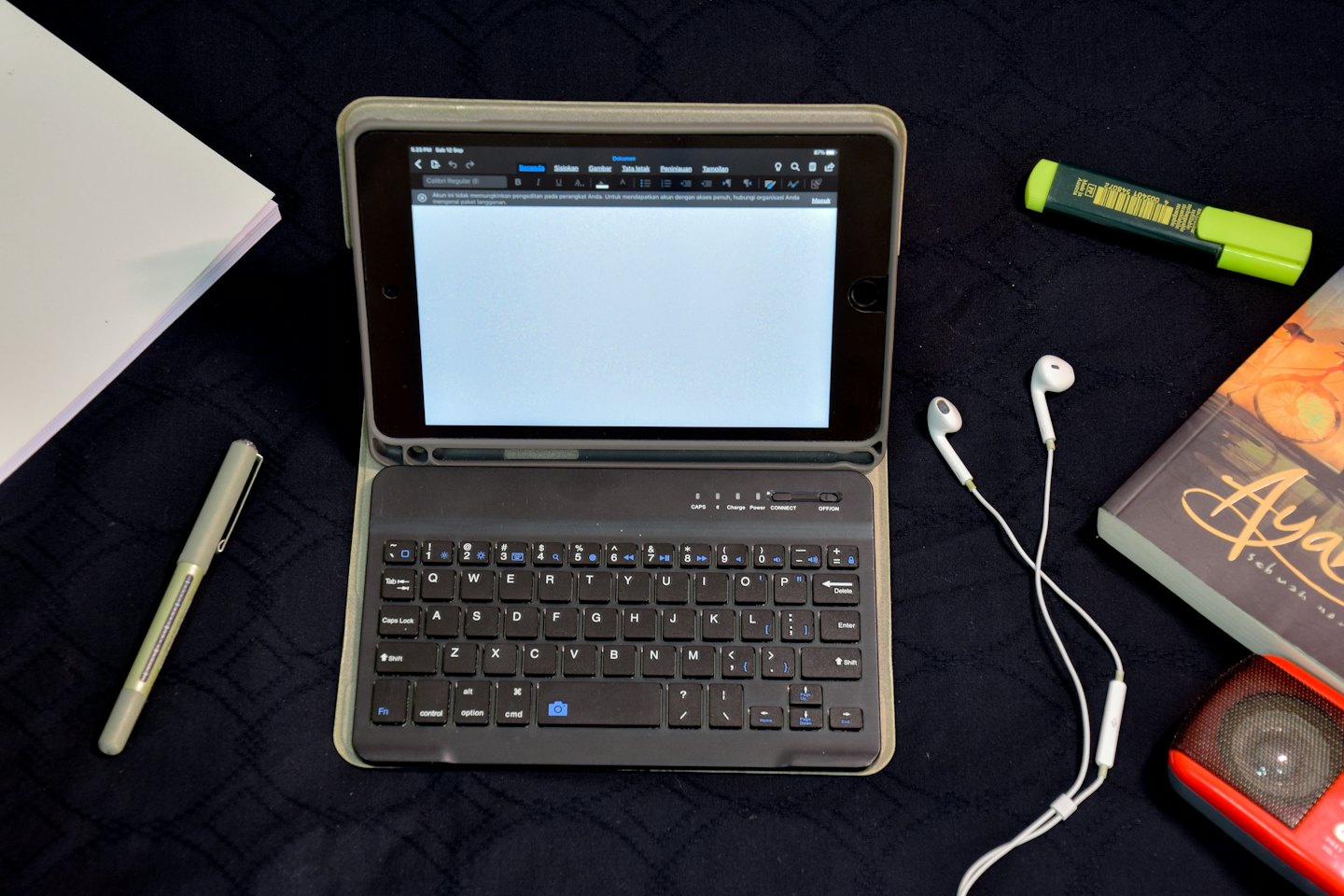 Tablet, pen, and office supplies arranged on a dark surface.